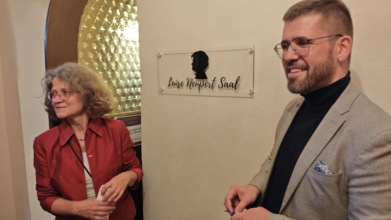Ein Abend voller Erinnerungen an Luise Neupert | Angela Kiesewetter-Lorenz (Freundeskreis Scherenschnitt) und Bürgermeister Sven Schrade enthüllen das neue Schild für den Luise Neupert Saal.