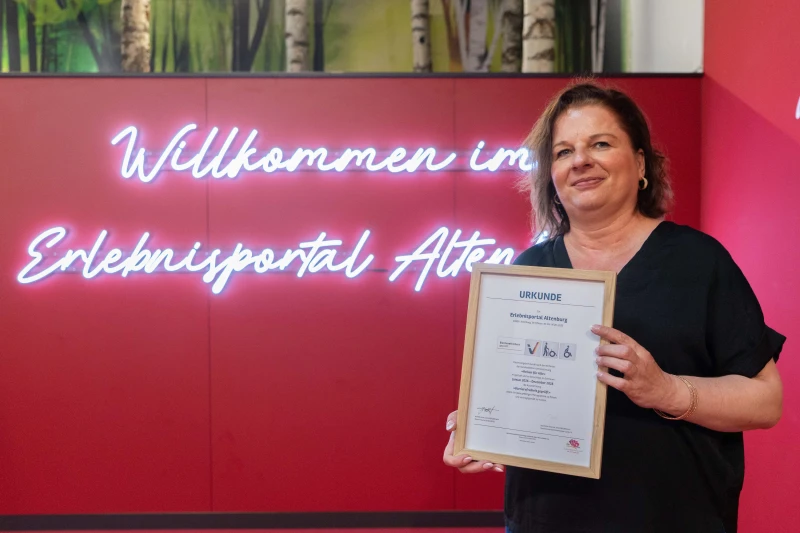 Altenburgs Erlebnisportal am Markt 2: Barrierefreiheit offiziell bestätigt | Frances Zeising, Mitarbeiterin im Erlebnisportal, zeigt die Auszeichnung.