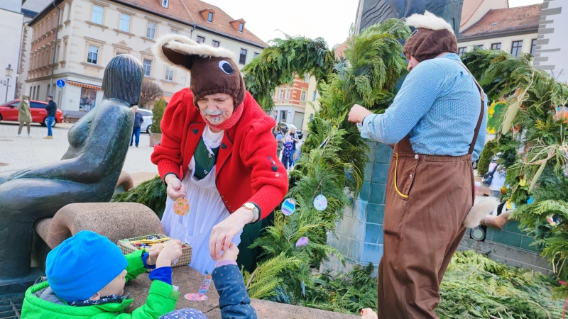 Osterbrunnengestaltung in Schmölln hat Tradition | Zwei mannsgroße Osterhasen nehmen am Brunnen Basteleien der Kinder entgegen.
